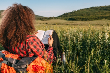 Back view of teenage girl reading book on a meadow